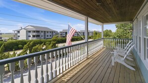 A wooden porch with a railing, a flag, and a view of a building complex.
