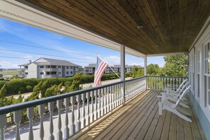 Une véranda en bois avec une balustrade, un drapeau et une vue sur un ensemble de bâtiments.