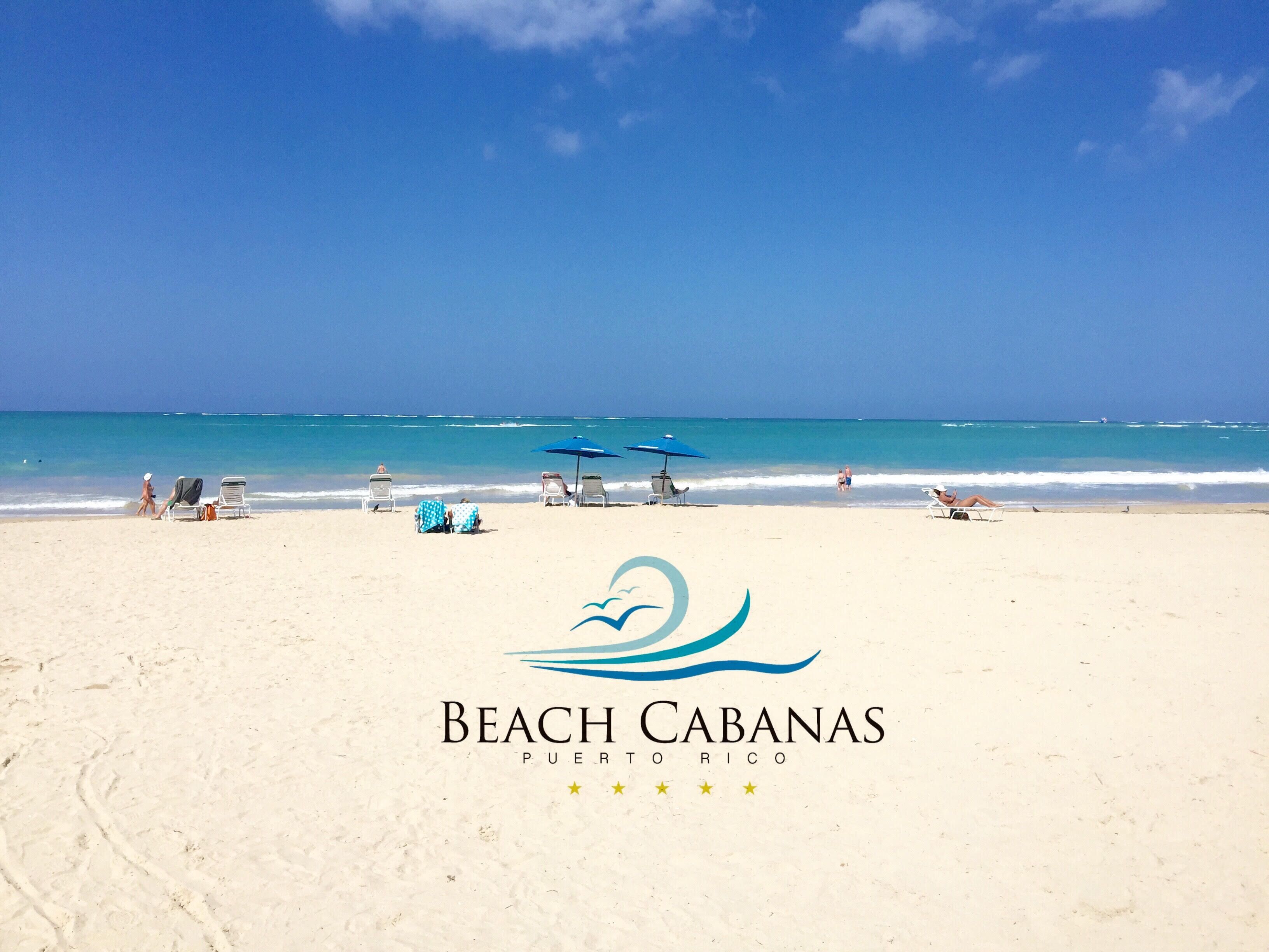 A beach with clear skies, a logo for Beach Cabanas Puerto Rico, and several sun loungers and umbrellas.