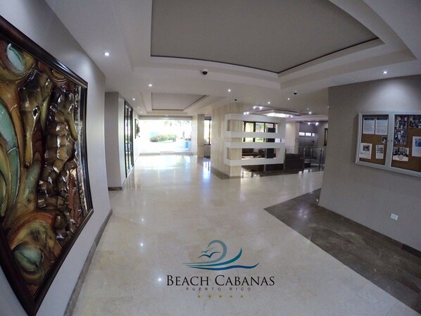 A modern hotel lobby with a large abstract painting, a reception desk, and a bulletin board.