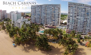 Un hotel frente a la playa con varios edificios altos, palmeras y cielo despejado.