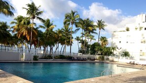 Zona de piscina con palmeras, sillas de descanso y un edificio blanco con la leyenda "Beach Cabanas Puerto Rico".