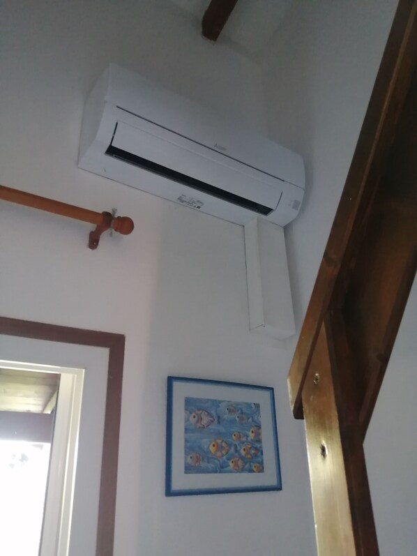 Un equipo de aire acondicionado montado en una pared blanca, un marco de puerta de madera y un cuadro con peces.