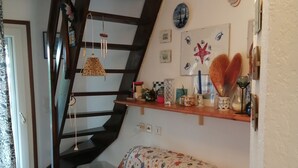 Un salon chaleureux avec un canapé à motifs floraux, un escalier en bois et un mur décoré de divers objets, notamment un vase en forme de cœur et des tableaux encadrés.
