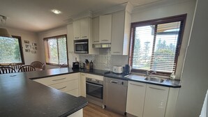 A modern kitchen with white cabinets, a black countertop, a microwave, a toaster, and a sink. - Parkview 1 Coastal 3 bedroom home,100m stroll to the beach, parks, cafés (Black Head)