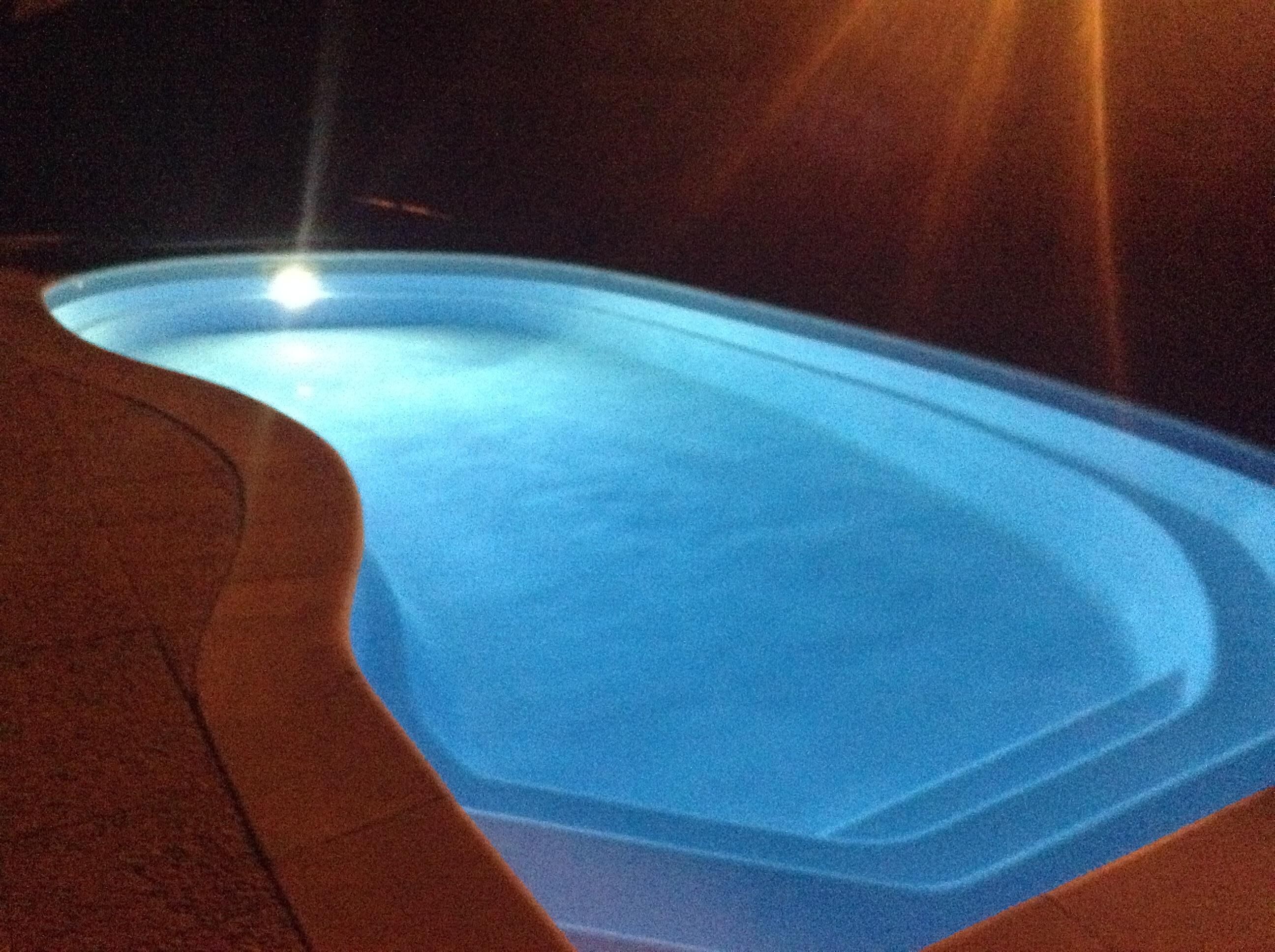 A swimming pool at night with a light source at the far end.
