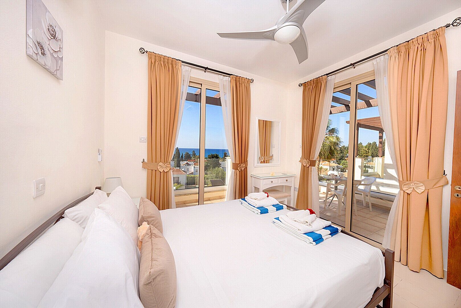 A hotel room with a bed, a desk, a chair, and a balcony with curtains.