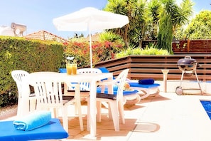 Área de piscina com mesa, cadeiras, churrasqueira e espreguiçadeiras.