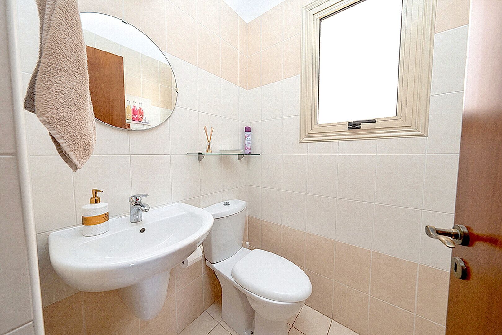 A bathroom with a white sink, a toilet, a mirror, and a window.