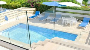 A clear view of a swimming pool with lounge chairs and umbrellas, surrounded by a landscaped garden. - Villa Jasmin (Coral Bay)