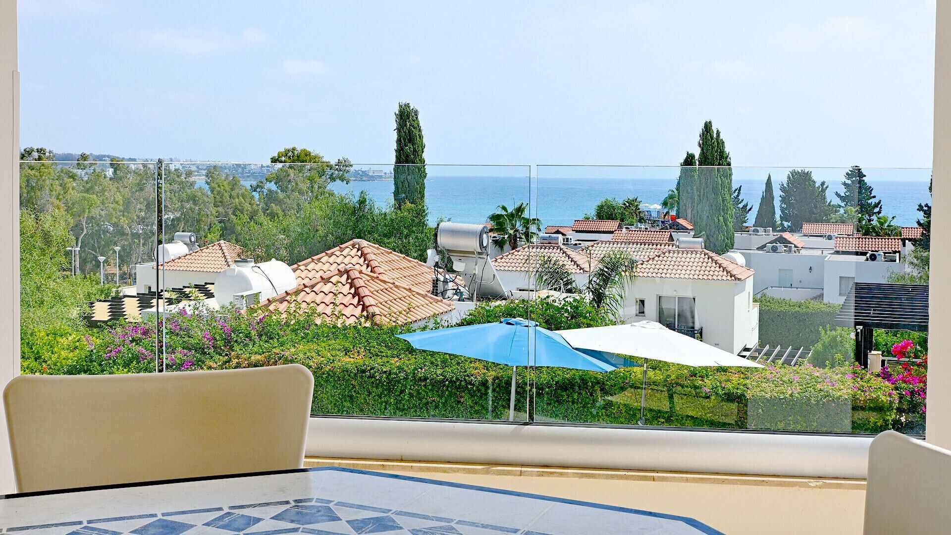 A balcony with a clear view of a coastal town, featuring terracotta-roofed buildings and lush greenery.