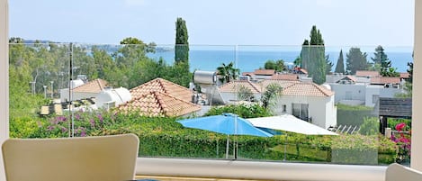 A balcony with a clear view of a coastal town, featuring terracotta-roofed buildings and lush greenery.