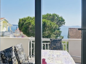 Un balcón con mesa y sillas, con vistas a una zona costera con árboles y un edificio al fondo.