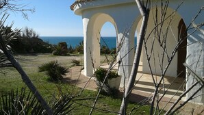 Un bâtiment situé sur la côte, doté d’une façade blanche, d’un toit recouvert de tuiles et offrant une vue sur la mer.