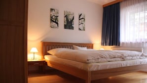 A wooden bed in a room with a nightstand, a lamp, and three tree paintings on the wall. - Quiet in the center: apartments The ideal basis for outdoor activities (Oetz)