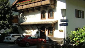 A traditional Alpine building with a balcony adorned with red flowers, a sign indicating 'Brunnfeldweg', and a clock on the facade. - Quiet in the center: apartments The ideal basis for outdoor activities (Oetz)