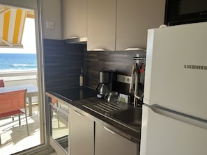 Cozinha moderna com fogão embutido, pia e geladeira. Vista para o oceano através de uma porta de vidro deslizante.