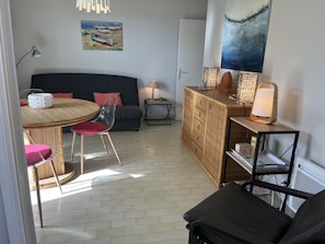 Een gezellige woonkamer met een ronde eettafel, transparante stoelen, een donkere bank, een houten kast en een boekenkast.