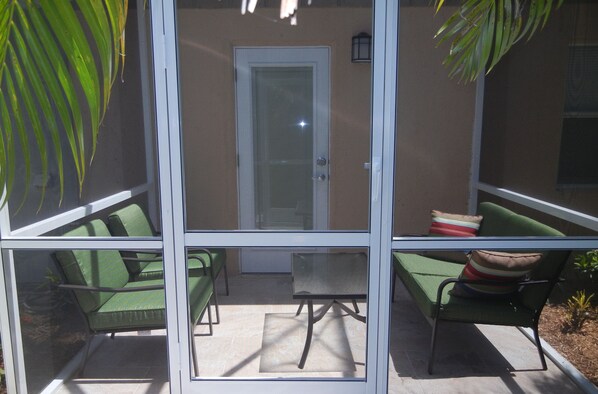 A screened porch with green chairs and a table, a door, and a small plant in the foreground. - Small But Cute 1/1 In A Tropical Oasis, Close To Siesta Beach (Sarasota)