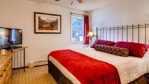 A hotel room with a bed, a television, a ceiling fan, a window with red curtains, and a framed picture on the wall. - Eagle Point Resort Vail Condo available December 18-25, 2026 (Vail)