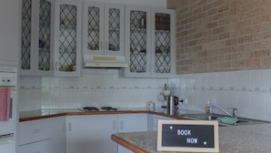 A kitchen with white cabinets, a granite countertop, a stainless steel kettle, and a sink. - A short walk to Black Head Beach, park with bbqs & amenities, shops and cafes (Black Head)