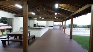 Eine überdachte Außenpatio mit Küchenbereich, Picknicktischen und Blick auf einen Swimmingpool.