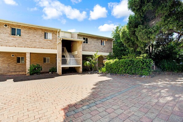 A two-story brick building with a covered outdoor area and a paved walkway.