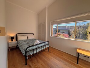 A bedroom with a bed, bedside table, lamp, window, and a bench.