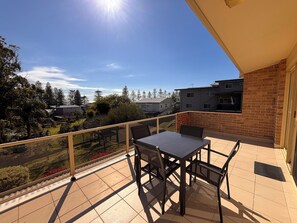 A balcony with a table and chairs, overlooking a residential area with houses and trees.