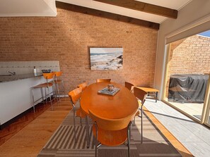 A dining area with a brick wall, a painting of a beach, and a view through a glass door.
