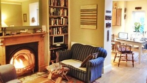 Ein gemütliches Wohnzimmer mit Kamin, einem gestreiften Sofa, einem Bücherregal und einem Essbereich mit Tisch und Stühlen.