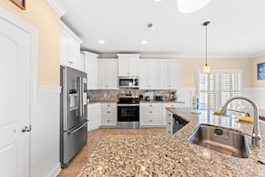 A modern kitchen with white cabinetry, stainless steel appliances, granite countertops, and a built-in oven. - Landshark, Luxury Oceanfront Cherry Grove Home with Game Room and Pool (North Myrtle Beach)