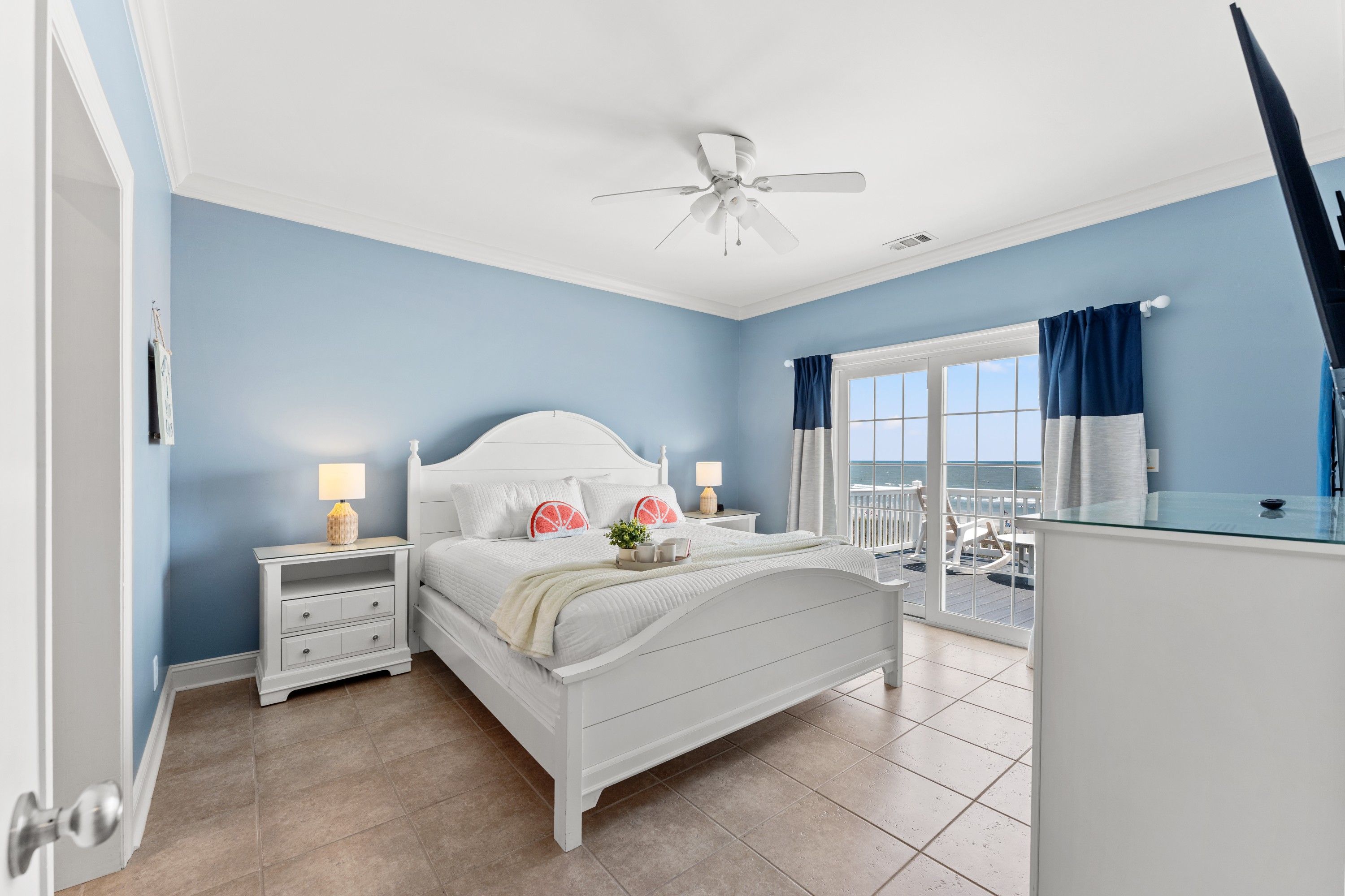 A bedroom with a bed, nightstands, a ceiling fan, and a view of the ocean through a window.