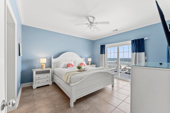 A bedroom with a bed, nightstands, a ceiling fan, and a view of the ocean through a window. - Landshark, Luxury Oceanfront Cherry Grove Home with Game Room and Pool (North Myrtle Beach)