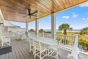 A covered outdoor seating area with a table and chairs, overlooking a beach. - Landshark, Luxury Oceanfront Cherry Grove Home with Game Room and Pool (North Myrtle Beach)