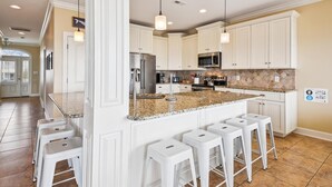 A modern kitchen with white cabinetry, granite countertops, stainless steel appliances, and pendant lighting. - Landshark, Luxury Oceanfront Cherry Grove Home with Game Room and Pool (North Myrtle Beach)