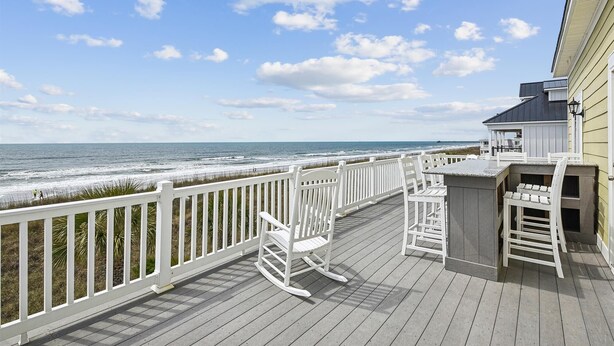 A wooden deck with white railings overlooking the ocean, featuring a bar area and seating. - Landshark, Luxury Oceanfront Cherry Grove Home with Game Room and Pool (North Myrtle Beach)