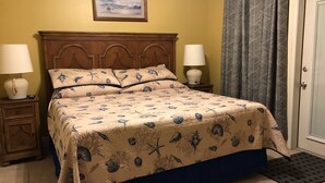 Ein Bett mit einem Wellendesign auf der Bettdecke, zwei Nachttischlampen, ein Holz-Kopfstück und ein gerahmtes Bild darüber.