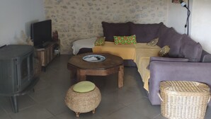 A cozy living room with a stone-patterned wall, a sofa set, a television, a fireplace, and a lamp. - house for 4 to 6 persons fenced garden (Sainte-Jalle)