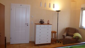 A room with a white door, a dresser with drawers, a small stool, a chair with a blanket, and a floor lamp. - Limburg: TOP apartment 75 sqm with balcony in quiet vorz. location (Limburg an der Lahn)