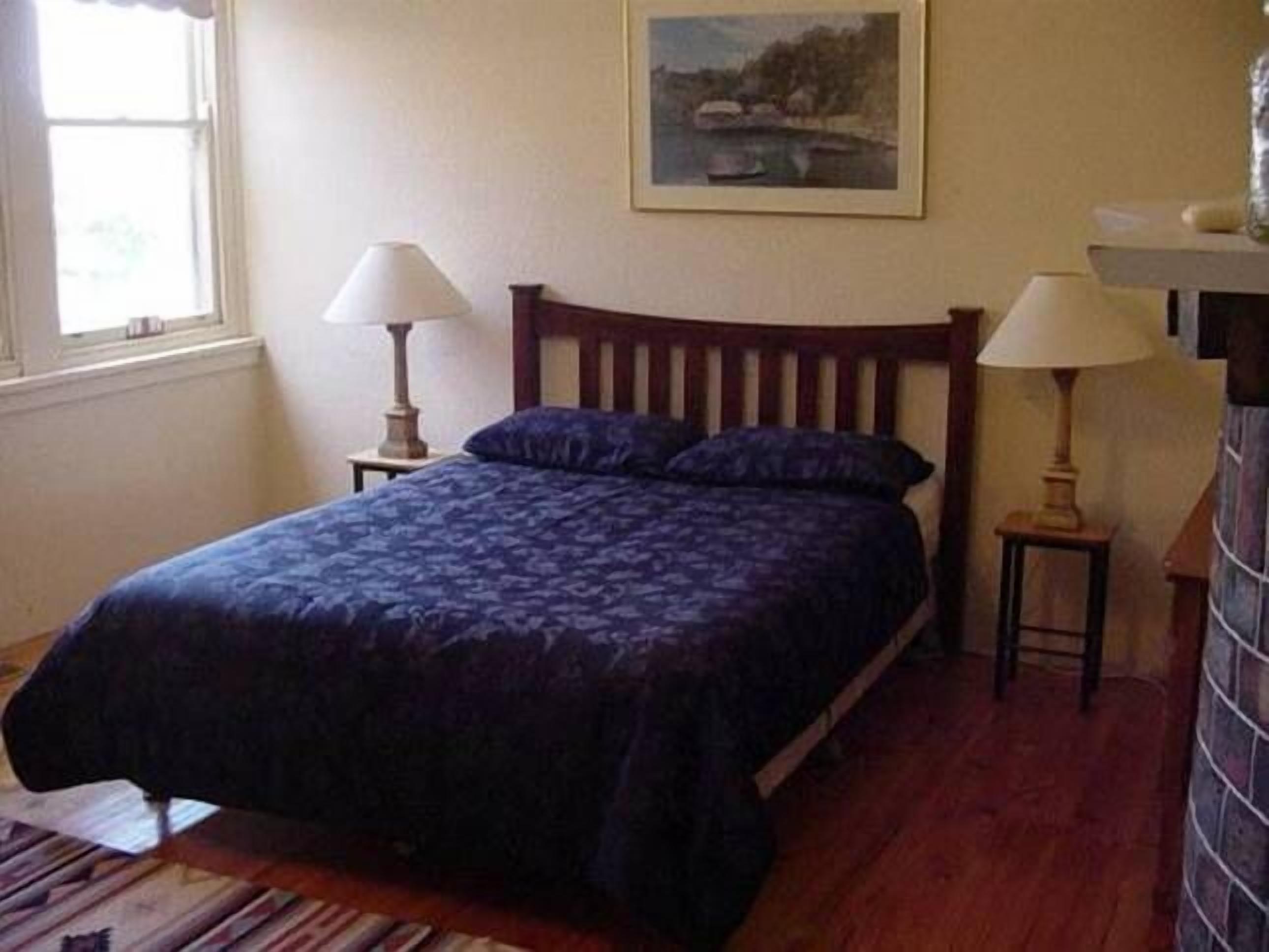Een slaapkamer met een bed, twee nachtkastjes, een raam en een schilderij aan de muur.