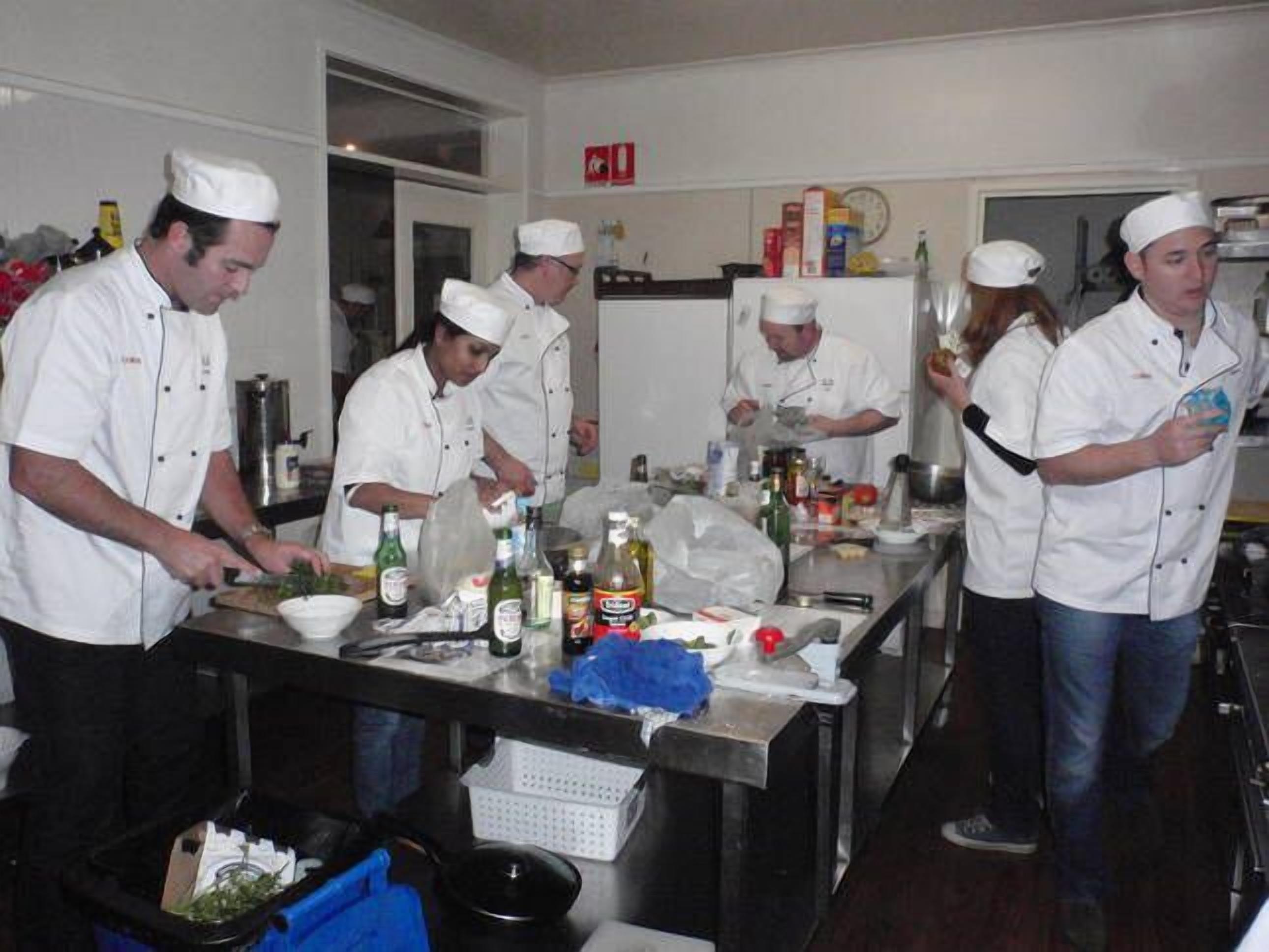 Una cocina profesional con cocineros preparando alimentos, equipada con diversos utensilios de cocina e ingredientes.