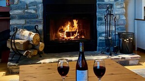 Una chimenea con revestimiento de piedra, una obra de arte enmarcada encima y dos copas de vino tinto sobre una mesa de madera.