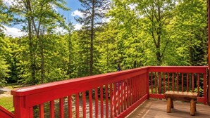 Una terraza de madera con barandilla roja, rodeada de frondosos árboles verdes.