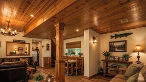 Un interior de cabaña con techo de madera, una zona de comedor y una sala de estar amueblada con sofás de cuero y mesas de madera.