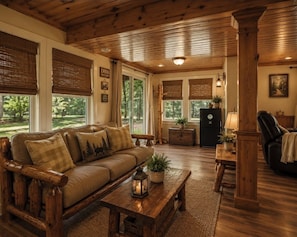 Interior de cabana com sofá de madeira, mesa de centro, lareira e mesa de jantar.