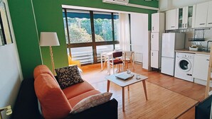 Un espacio habitable compacto con sofá, mesa de comedor, sillas, lavadora y zona de cocina.