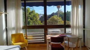 Una habitación con mesa de comedor, sillas amarillas y blancas, un sofá y ventanas grandes con cortinas.