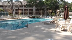 A swimming pool with lounge chairs and umbrellas, surrounded by a fence and trees. - 1st Floor, Updated, 5 min walk to the beach! (Hilton Head Island)