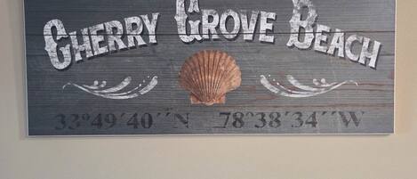 Un panneau en bois portant l’inscription « Cherry Grove Beach » et les coordonnées « 33°49'40''N 78°38'34''O ».